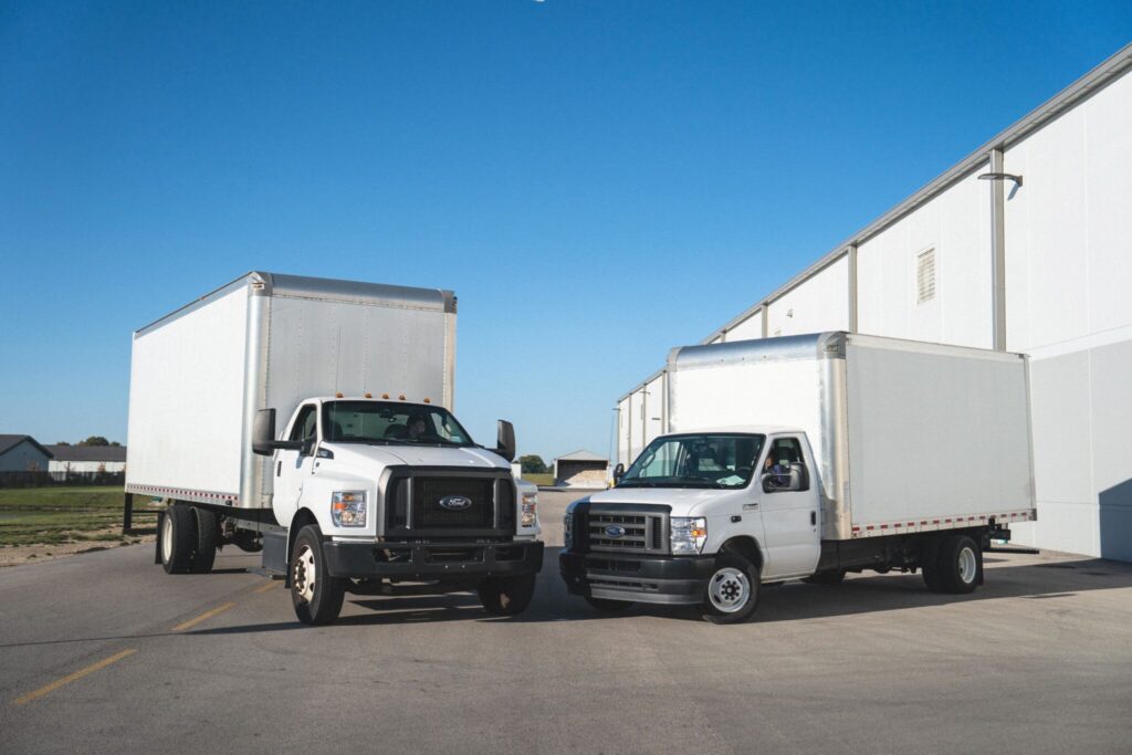 Two white Ford box trucks parked side by side on asphalt lot