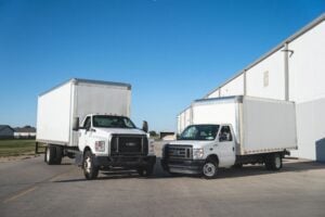 Two white Ford box trucks parked side by side on asphalt lot