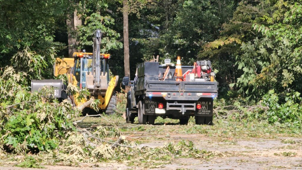A backhoe and a work truck clear fallen tree limbs from a Greenville street