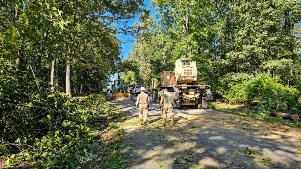 South Carolina Army National Guard soldiers walk a Greenville road lined with downed trees as a loader and a crane truck clear debris