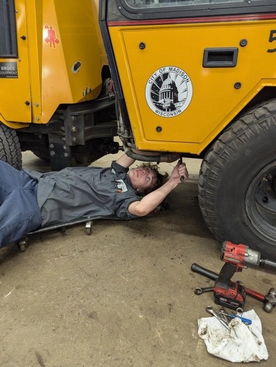 Fleet technician Luc Meuzelaar working under a City of Madison public works tractor