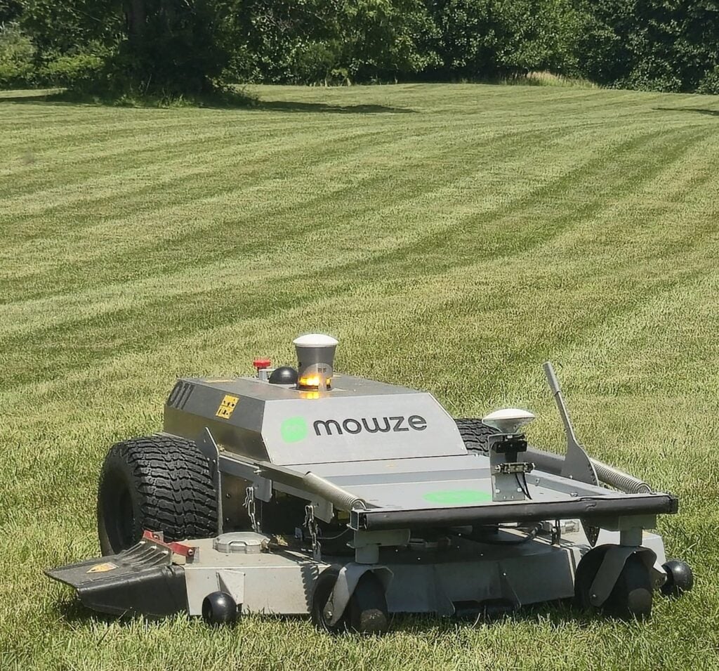 Mowze autonomous lawn mower operating on striped grass field with trees in background