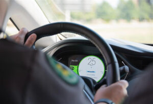 Driver's hands on steering wheel with digital dashboard display showing speed of 25 mph