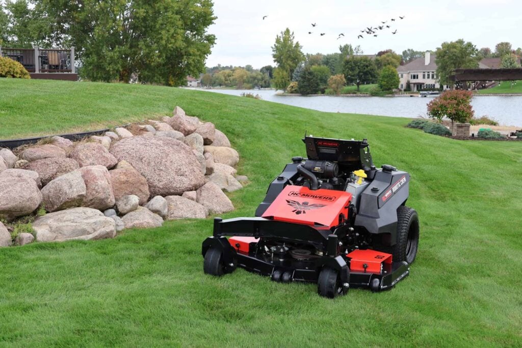 RC Mowers RECONX autonomous stand-on mower on a lawn beside a pond