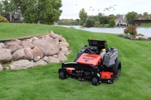 RC Mowers RECONX autonomous stand-on mower on a lawn beside a pond